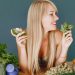 A smiling woman holding avocado and basil, surrounded by fresh vegetables and fruits for healthy eating.