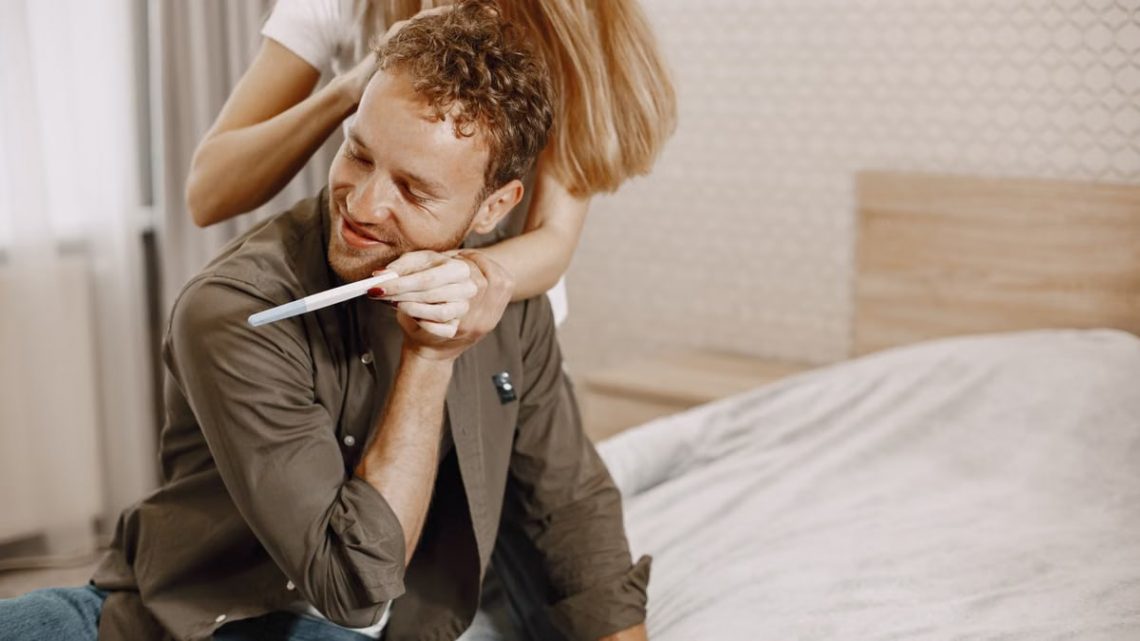 A happy couple celebrating after seeing a positive pregnancy test result in their bedroom.