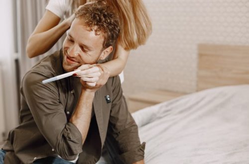 A happy couple celebrating after seeing a positive pregnancy test result in their bedroom.